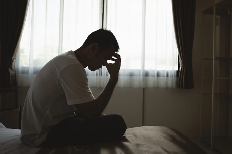 silhouette of a young man sitting sadly on a bed with his head in his hand