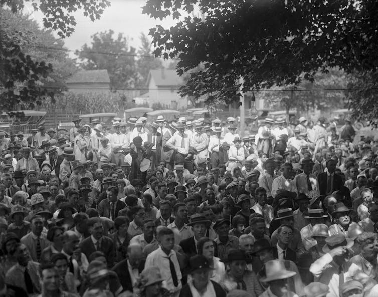 A large group of men and women standing outside, intently looking ahead.