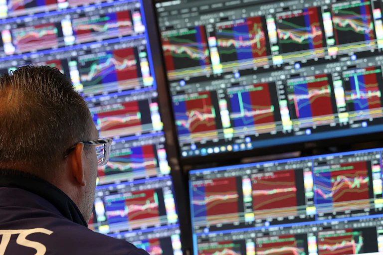 The back of a person's head is visible as the person looks at screens showing numbers and line charts of financial data.