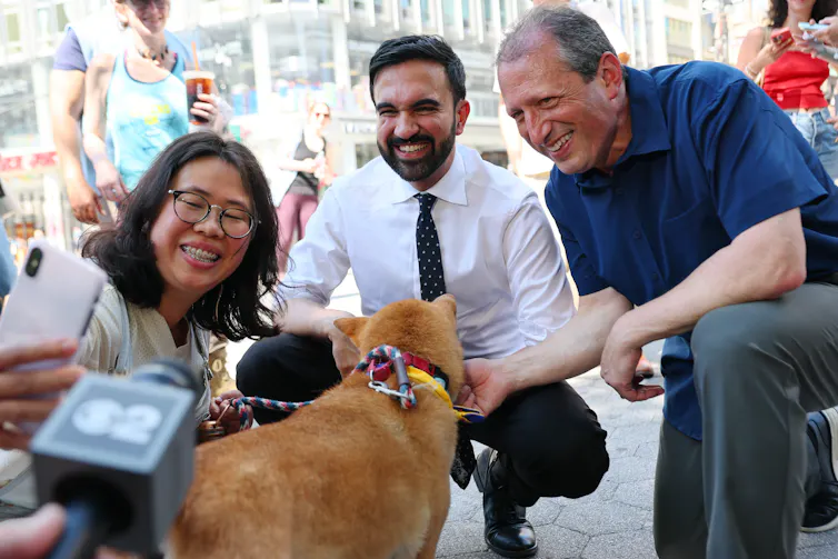 Two men kneel and smile, posing next to a woman and a dog.