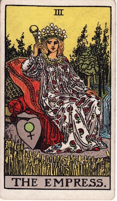 Por qué la astrología y el tarot de los siglos de edad todavía se sienten atraídos por 2 Un dibujo de una mujer en una capa roja y blanca. Ella se sienta en una silla