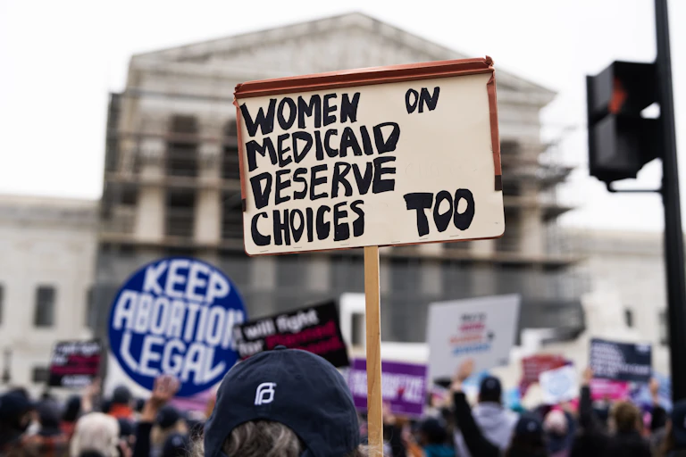 A protester holds a sign aloft that says 'Women on Medicaid deserve choices too,' with another sign in the background that says 'Keep Abortion Legal,'