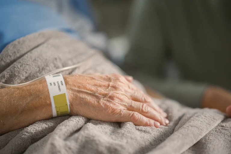 Hand of older person resting in hospital bed
