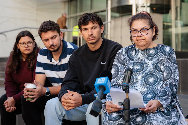 An Indigenous family sits in front of a court, giving an emotional speech.