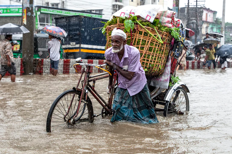 Bangladesh man pushing bike loaded with baskets through flooded road