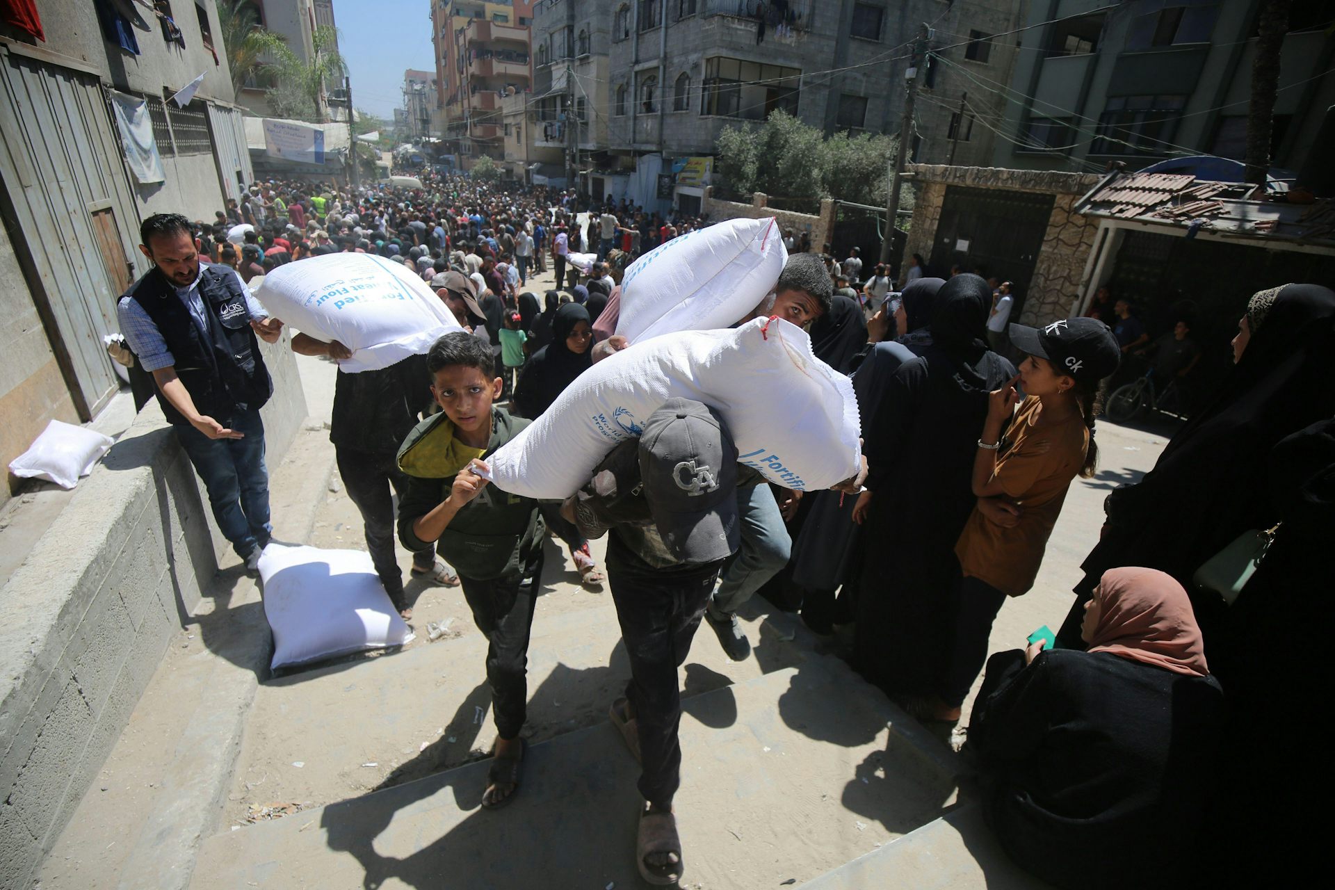 Palestinians carry sacks of foodstuffs away from aid distribution points in Gaza, June 2025.
