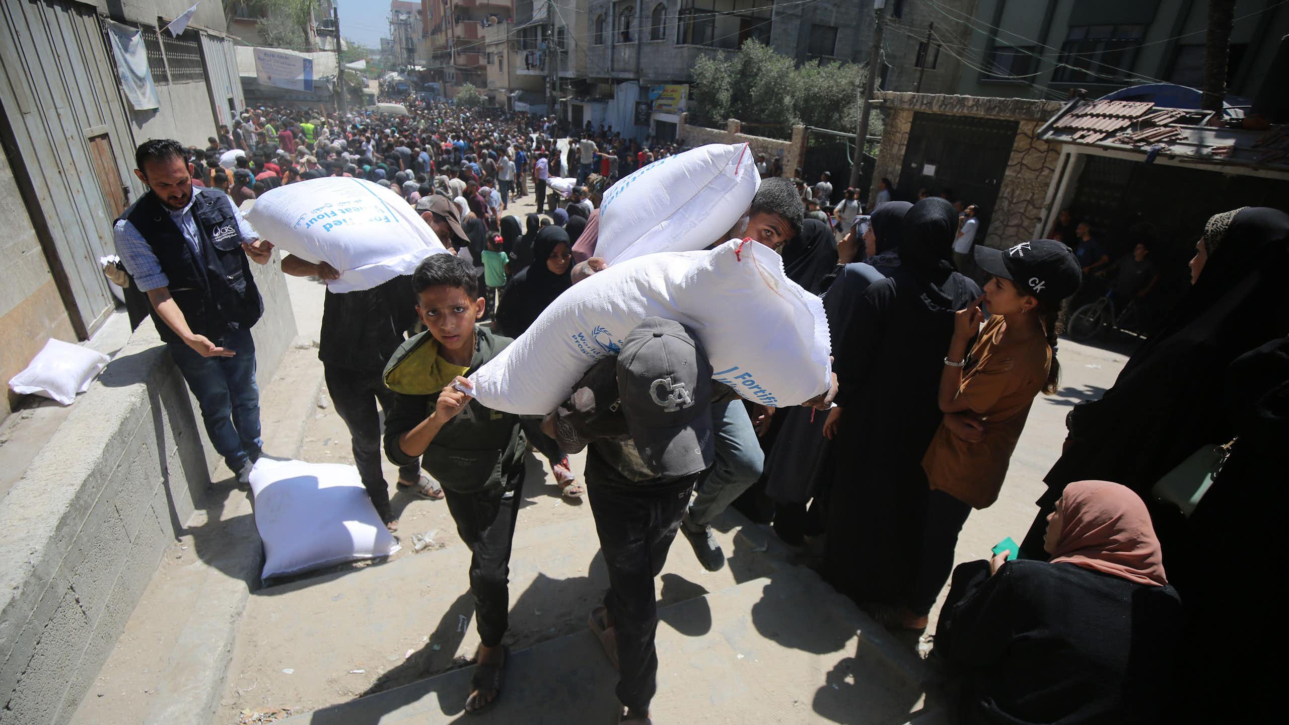 Palestinians carry sacks of foodstuffs away from aid distribution points in Gaza, June 2025.