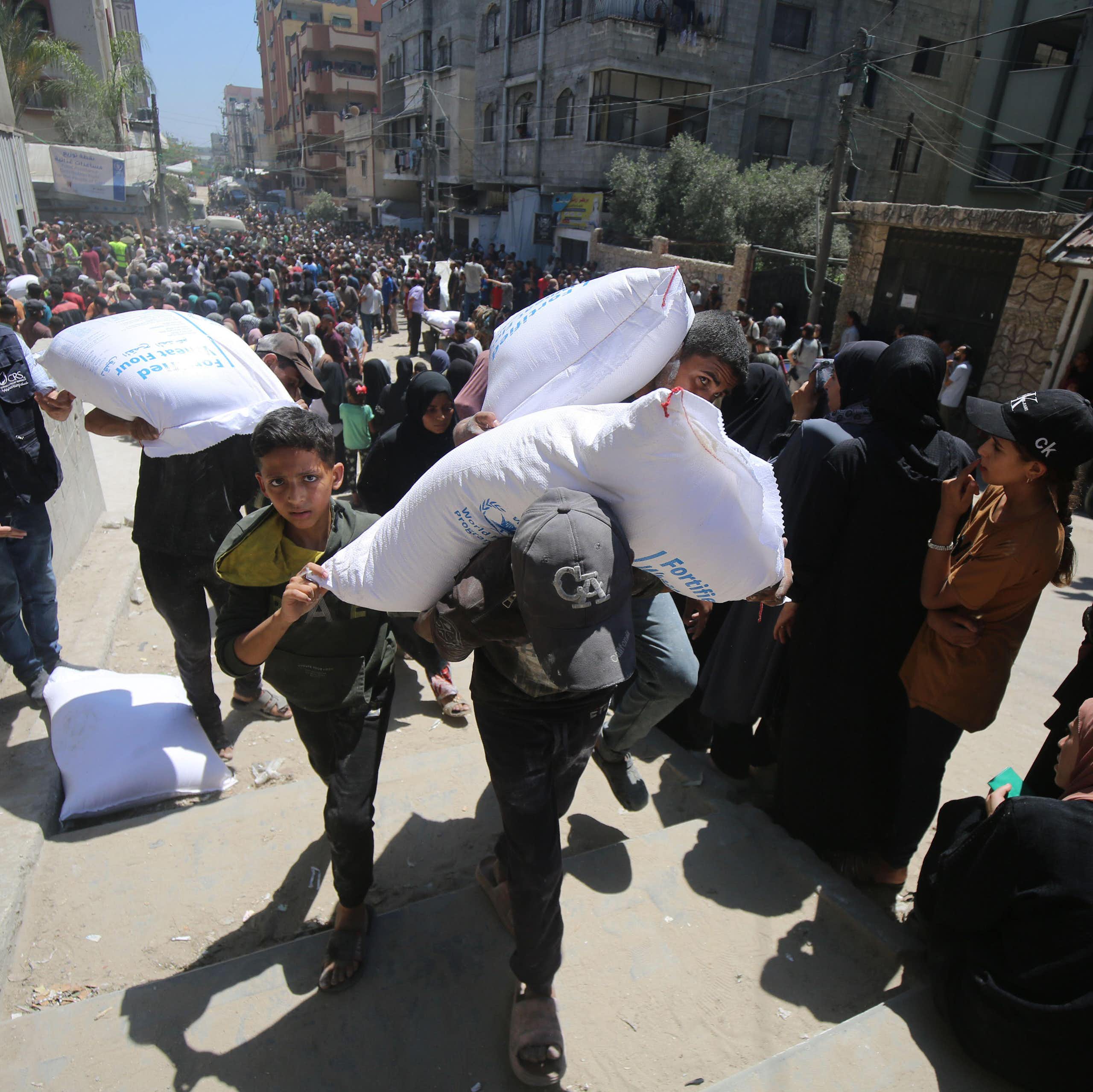 Palestinians carry sacks of foodstuffs away from aid distribution points in Gaza, June 2025.