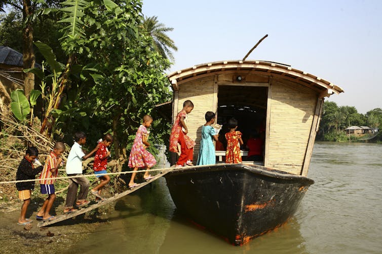 children in colourful clothing getting on to solar powered boat on river