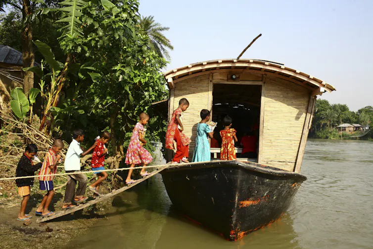 children in colourful clothing getting on to solar powered boat on river