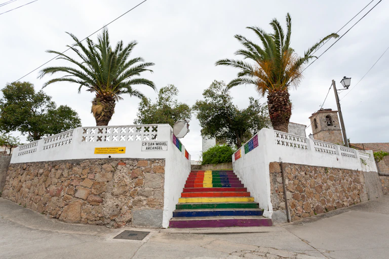 Escalera cuyos escalones los colores de la bandera LGTBIQ, flanqueada por palmeras
