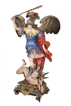 Escultura de un ángel venciendo a un demonio en el suelo.
