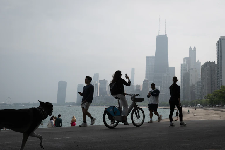 People bike and walk along the lake shore in Chicago while smoke shrouds the iconic downtown skyline.