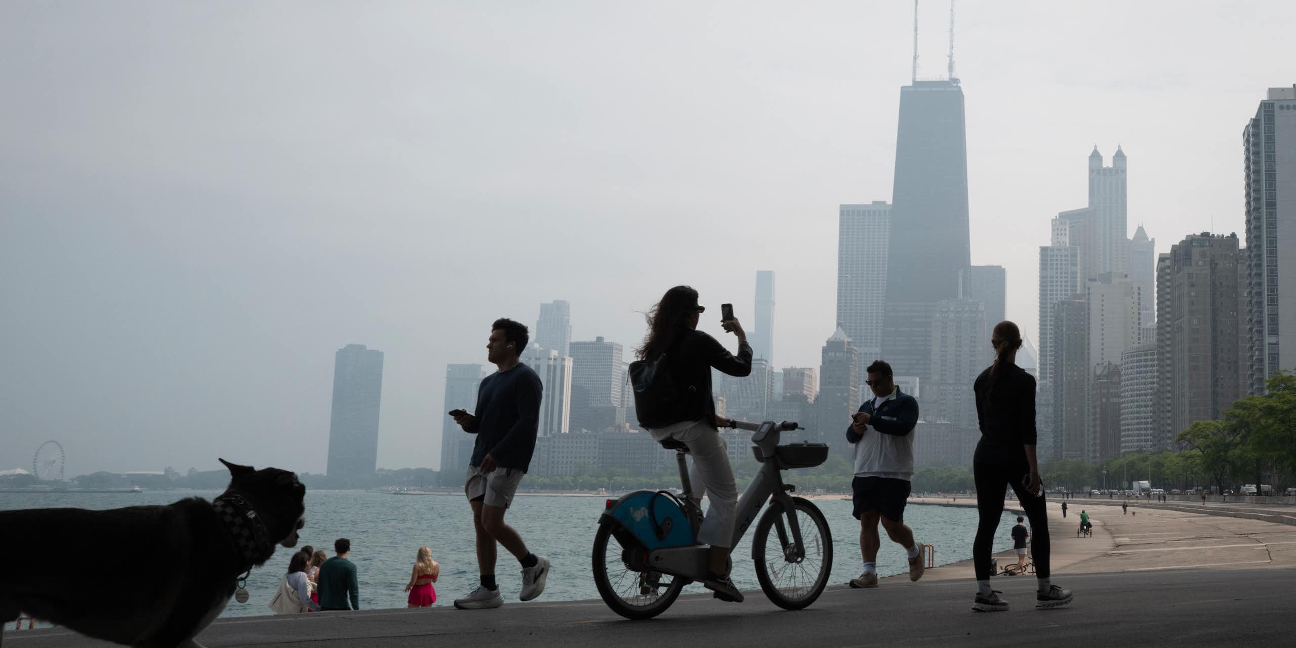 People bike and walk along the lake shore in Chicago while smoke shrouds the iconic downtown skyline.