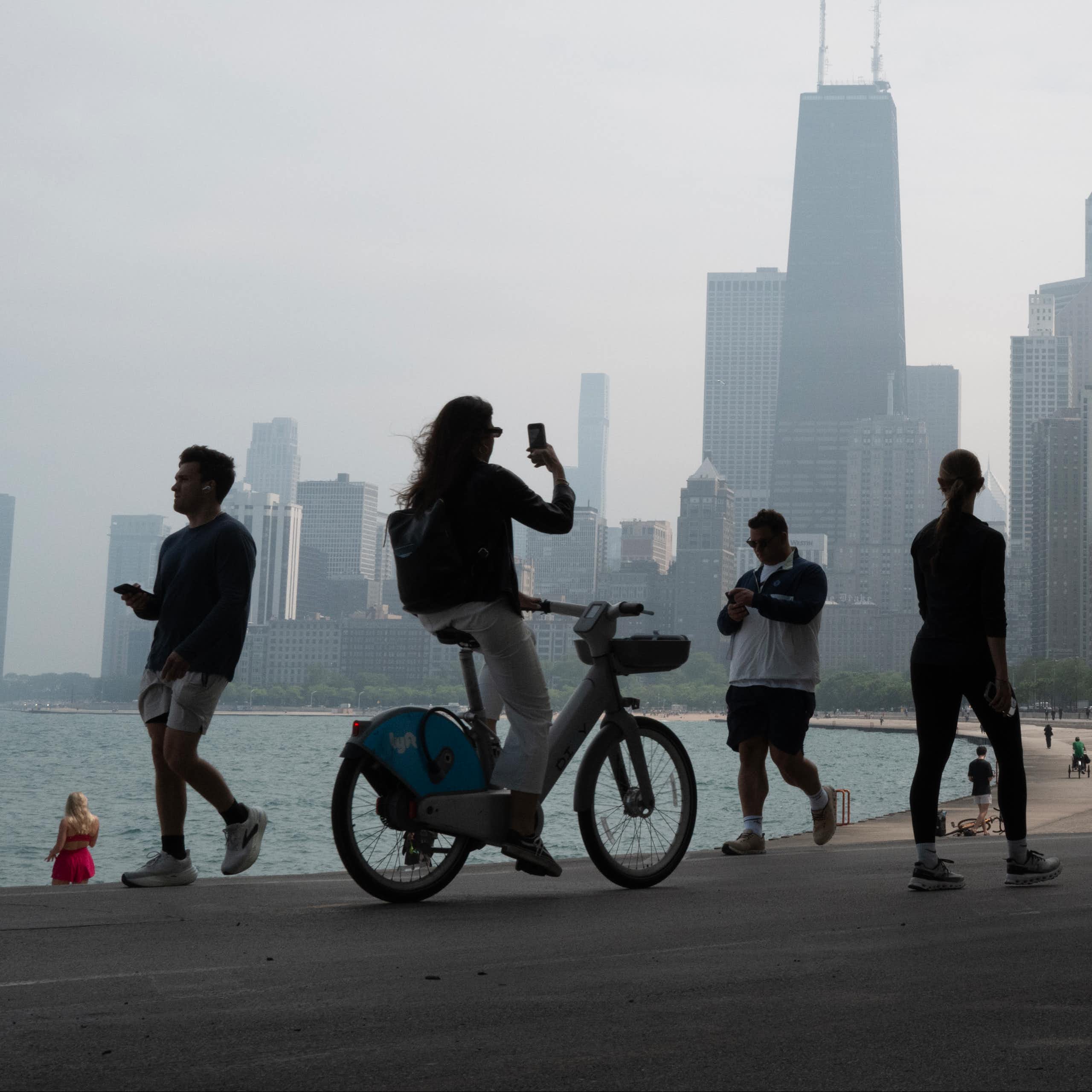 People bike and walk along the lake shore in Chicago while smoke shrouds the iconic downtown skyline.