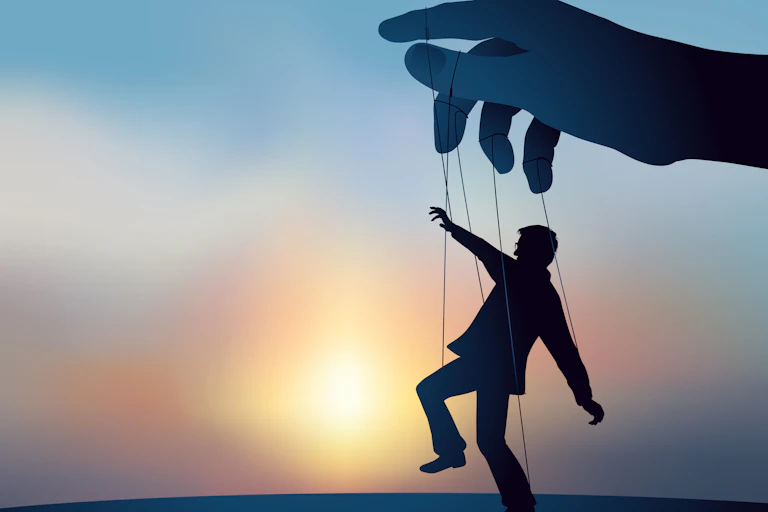 A silhouette of a gigantic hand manipulating a man connected to marionette strings.