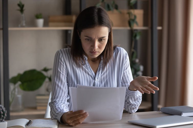 Los lugares de trabajo aceptaban cuidado y autocompensación, pero el capitalismo es un secuestro de su verdadero propósito? 1 La mujer mira el rayo de papel en sus manos con una mirada aburrida en su rostro