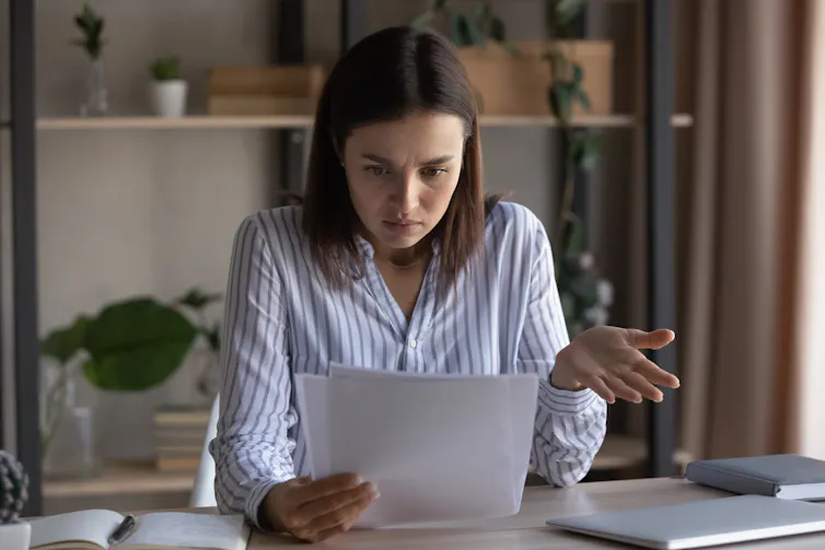 A woman looks down at a sheaf of papers in her hands with an annoying look on her face