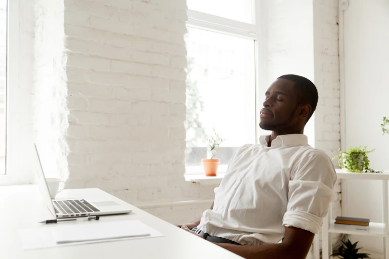 A man leans back at a desk with his eyes closed