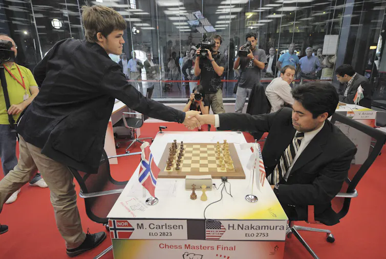two men in sports coats shake hands over a chessboard
