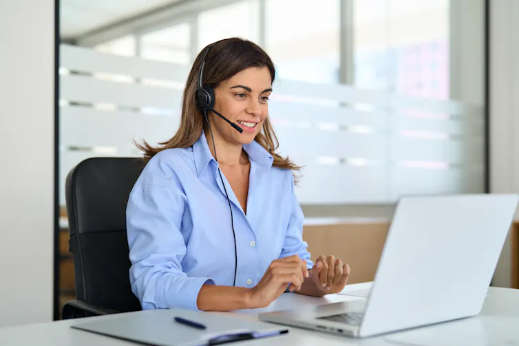 A woman wearing a headset smiles while working on a laptop