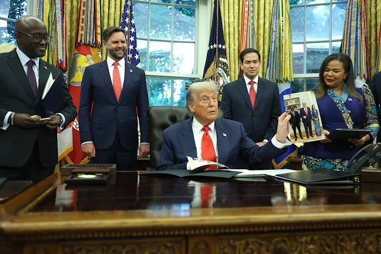 Three men and a woman standing behind a seated man who is speaking and holding up a photo of himself and two Africans, a man and a woman