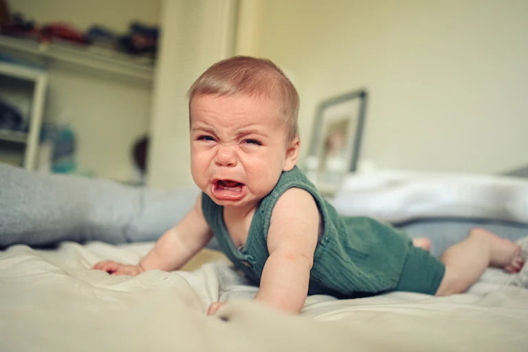 A baby on a bed, crying.