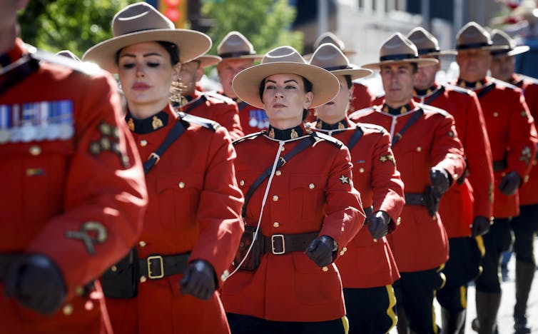 Hombres y mujeres en chaquetas y lutones en serie rojas marchan en un desfile.