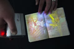 Nuevo pasaporte luminiscente en la mano con una luz infrarroja que brilla en él.