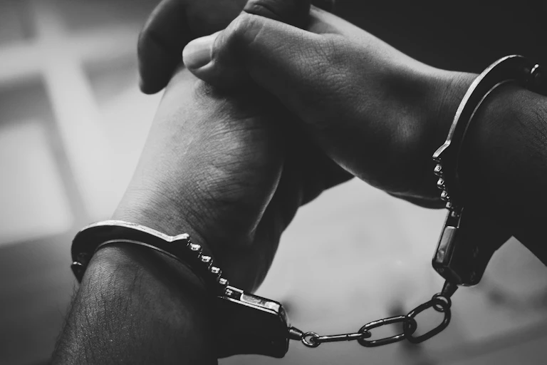 A black and white image shows a man in handcuffs.