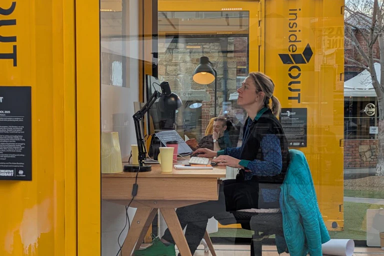 Woman at writing desk inside first glass box, man reading in chair inside second glass box