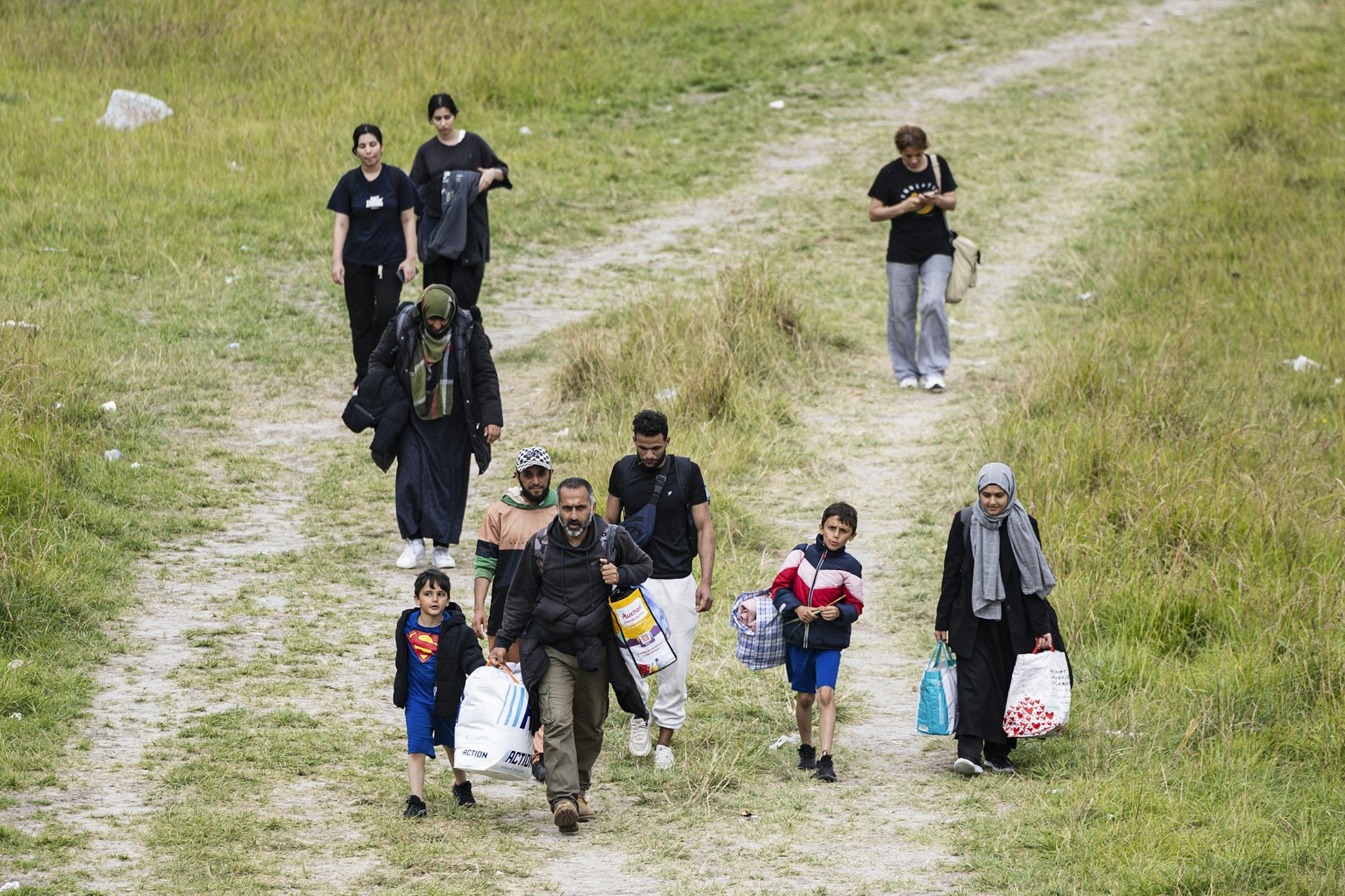 Des parents et leurs enfants marchent avec des sacs au milieu d'une zone herbeuse