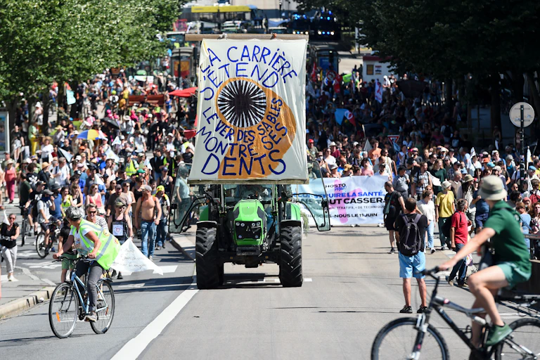 Manifestation avec des piétons, des véols et un tracteur avec une banderole sur on lit « La carrière s'agrandit, le ver des sables montre les dents »