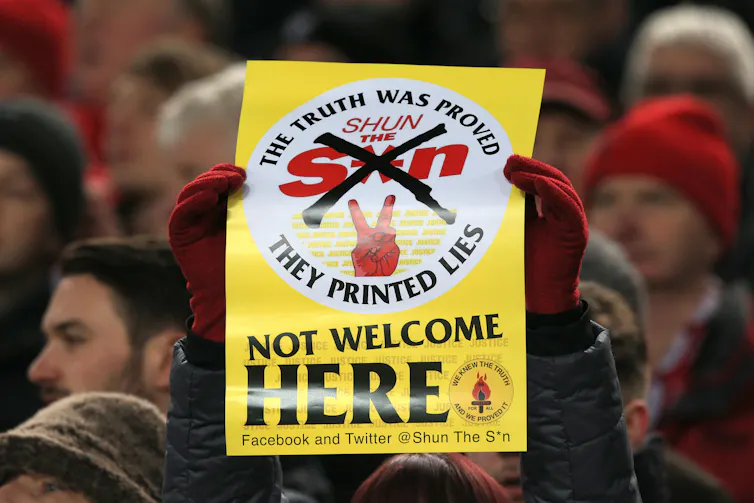 A Liverpool fan holds up a yellow sign proclaiming the Sun not welcome here