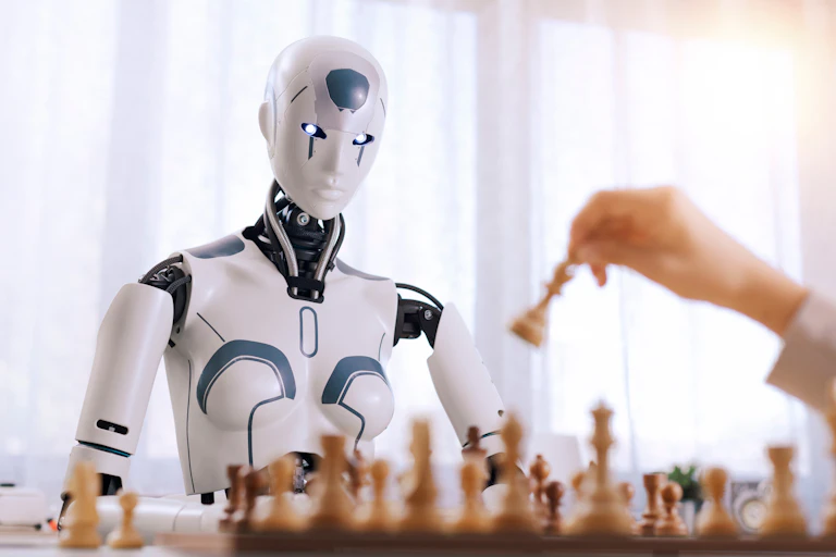 Una mano mueve una ficha de ajedrez frente a un robot sentado enfrente