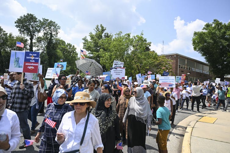 A protest outside, with people walking down a street as they carry placards.