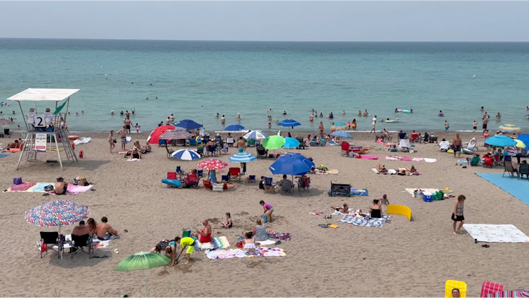 Imagen de playas con gente, paraguas, mantas y rescatistas