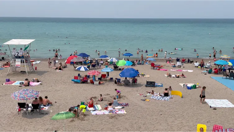 Photo of a beach with people, umbrellas, blankets and a lifeguard station
