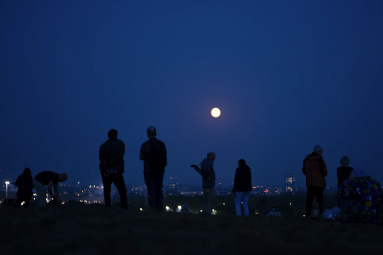 A group of people standing on a ridge, looking at the full Moon