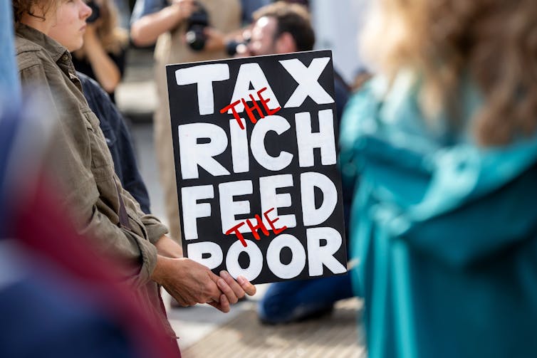protester holding a sign reading tax the rich feed the poor