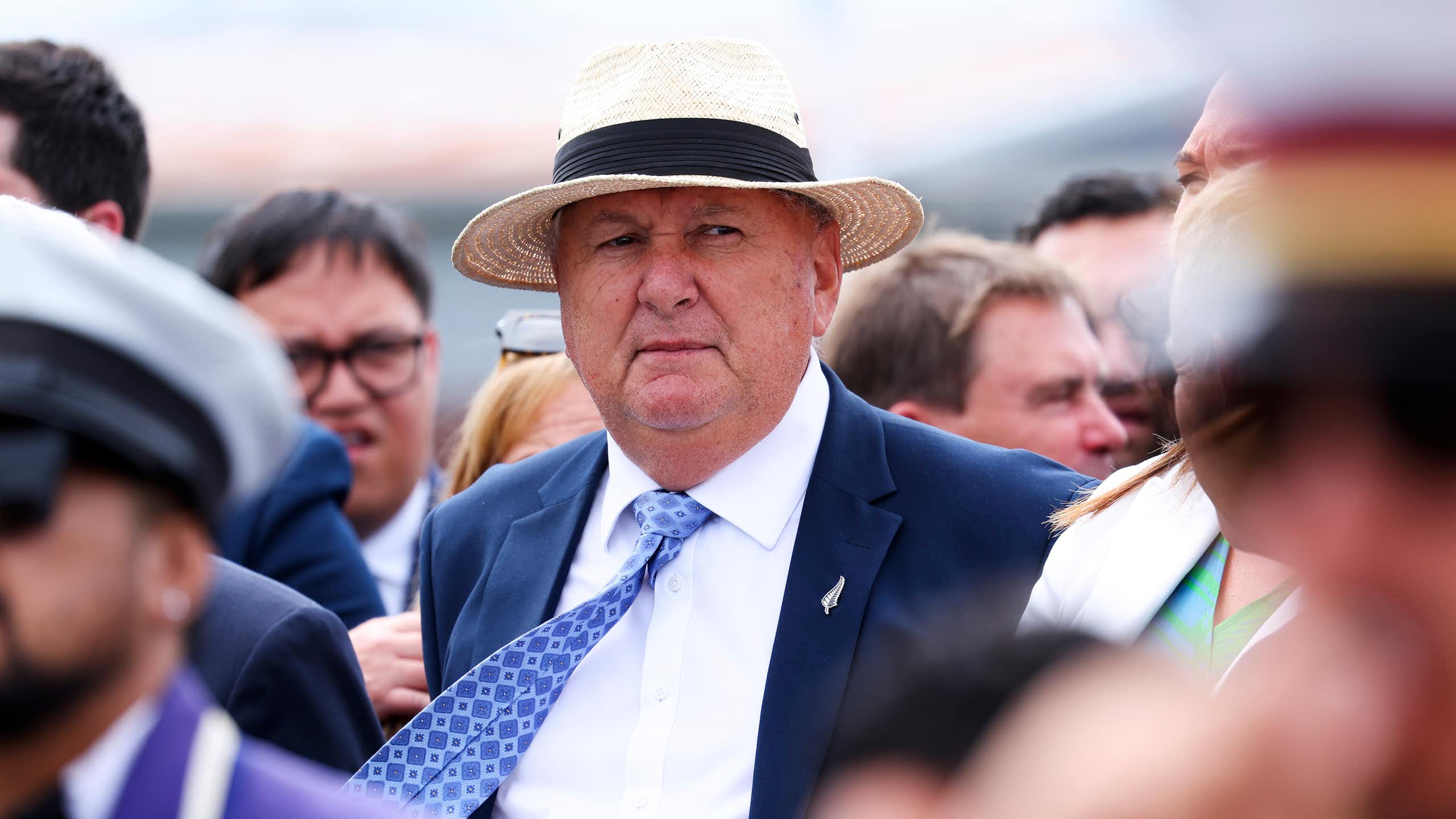 Man in suit, tie and hat standing among a crowd of people