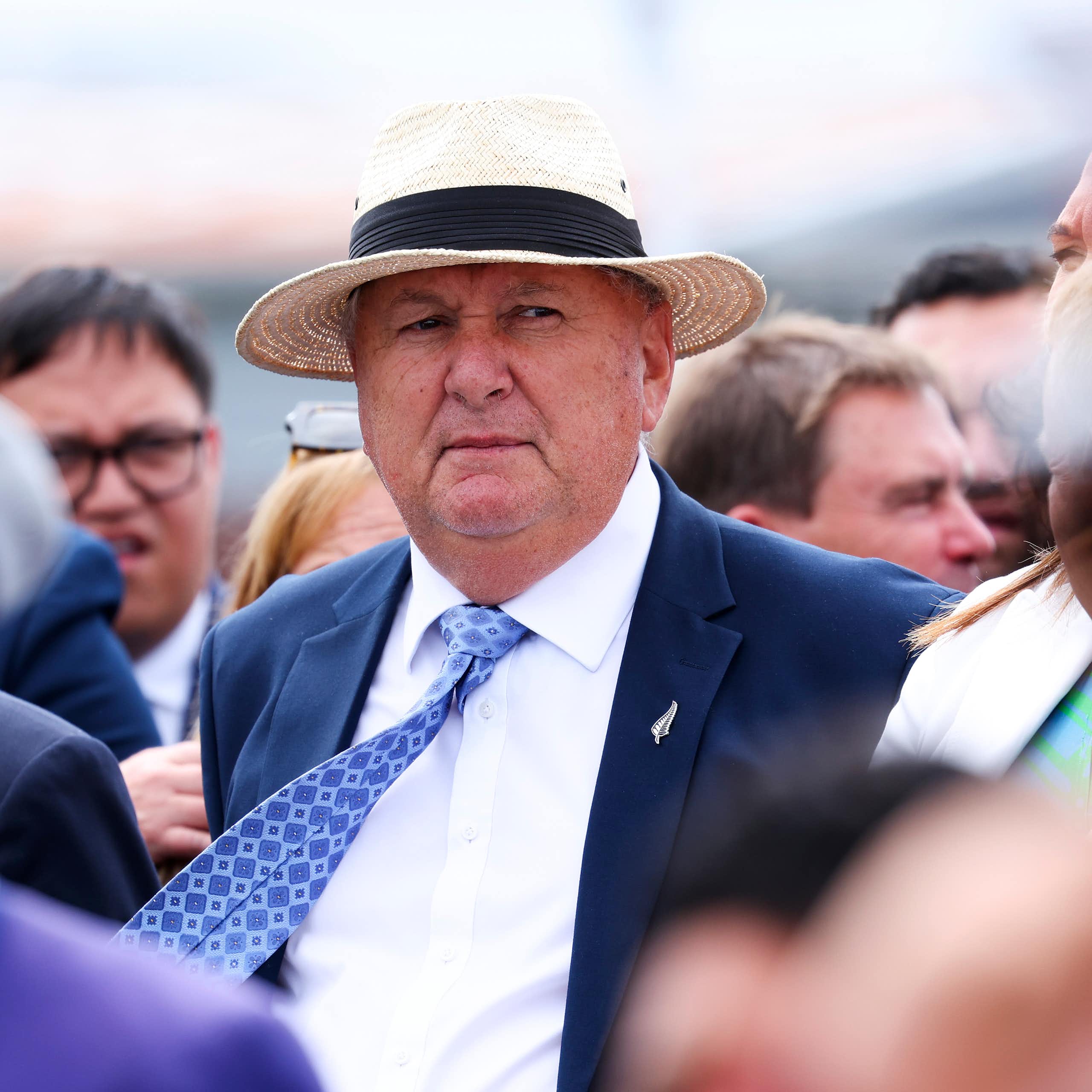 Man in suit, tie and hat standing among a crowd of people