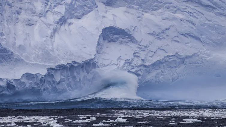 A wave hits the Antarctic ice sheet, causing ice to break off into the ocean