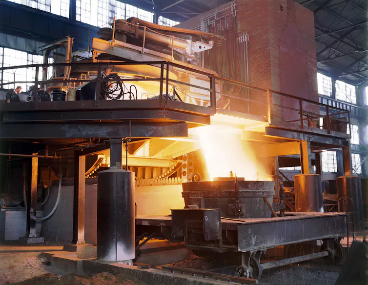 Bright hot metal pouring out of a large metal furnace.