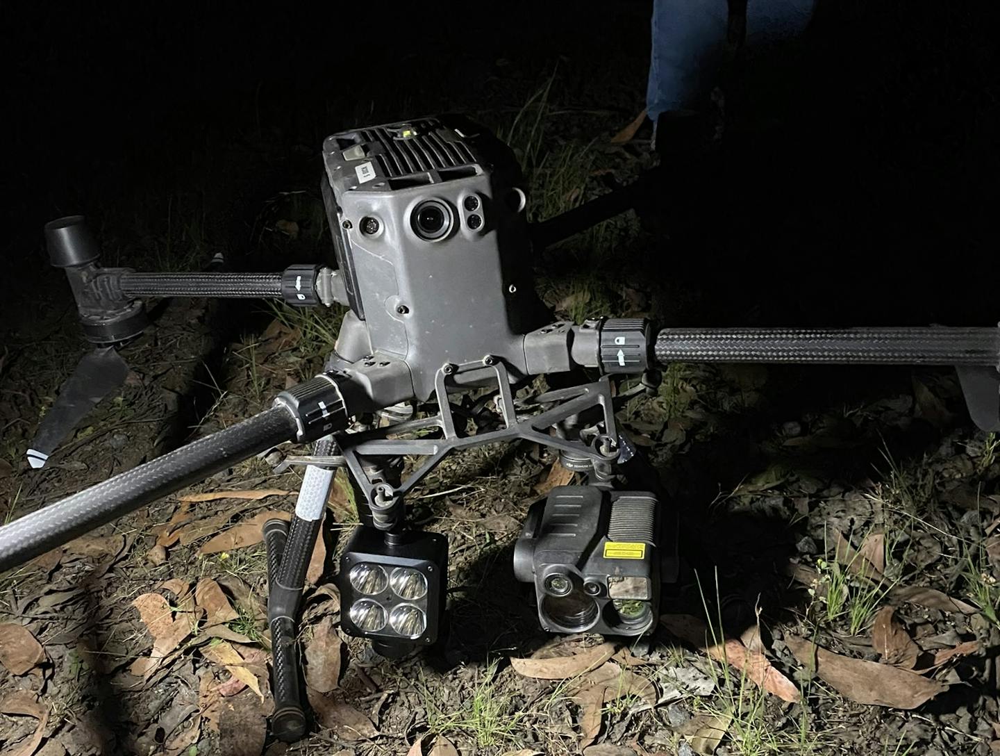 A grey drone with a light and a camera attached on the ground.