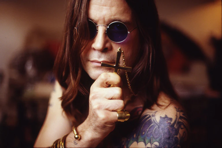 Osbourne holds a cross necklace up to the camera.