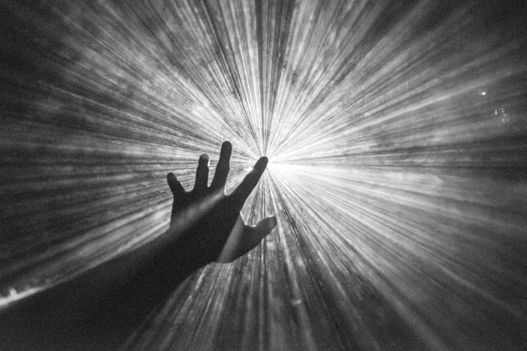 Hand reaching towards light beams.