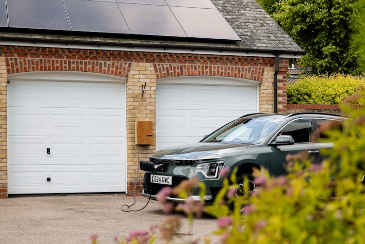 An electric car on a home driveway plugged into a charge point.