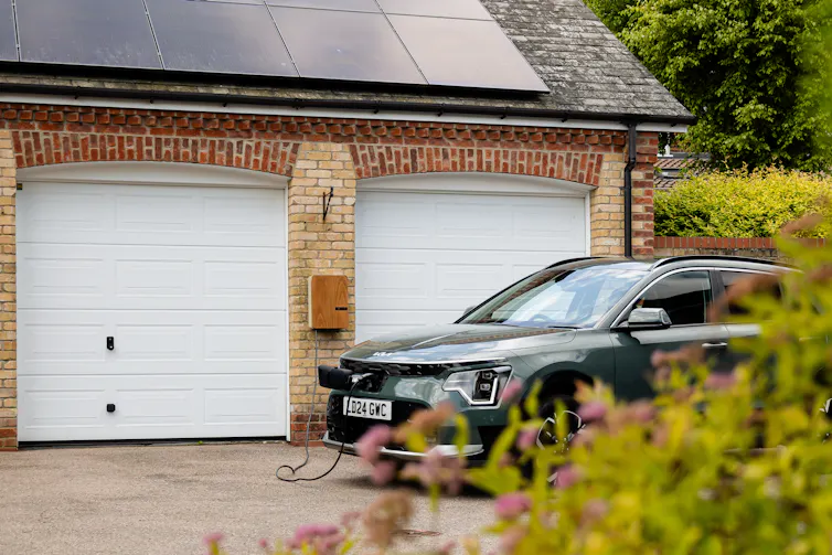 An electric car on a home driveway plugged into a charge point.