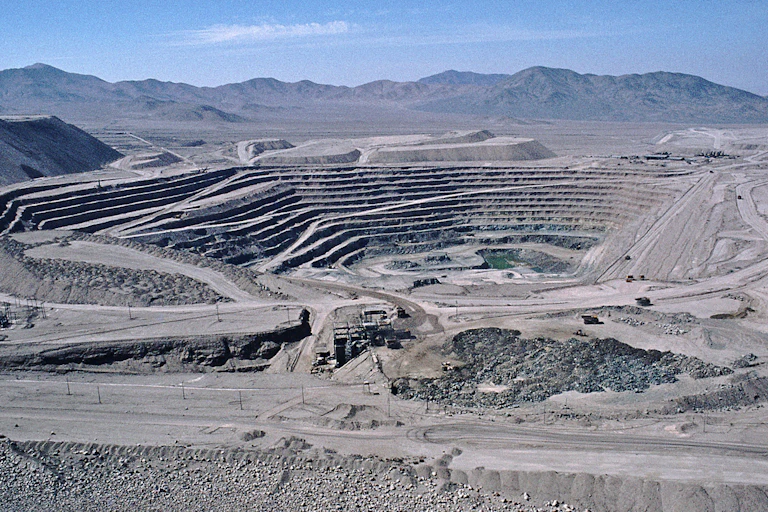 A large open pit in the landscape, terraced, dusty, with no plants